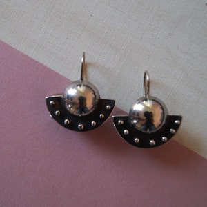 May include: A pair of silver earrings with a half-circle design and a round ball in the center. The earrings have a textured surface with small dots.
