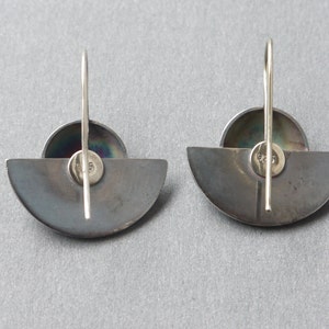 May include: A pair of silver earrings with a half-circle design and a small round iridescent stone in the center. The earrings have a simple hook closure.