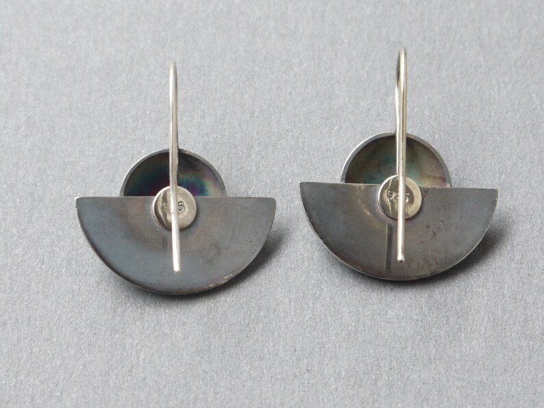 May include: A pair of silver earrings with a half-circle design and a small round iridescent stone in the center. The earrings have a simple hook closure.