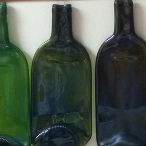 Peut inclure: Rangée de bouteilles de vin en verre recyclé aplaties, de différentes nuances de vert et d'ambre foncé. Les bouteilles sont montées sur un mur, mettant en valeur leur design unique et réutilisé. Les bouteilles ont une forme arrondie.
