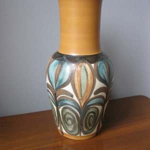 May include: A brown ceramic vase with a geometric pattern in shades of blue, green, and brown. The vase has a narrow neck and a wide base.