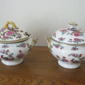 May include: Two white porcelain serving bowls with lids. The bowls are decorated with a floral pattern and colorful birds. The lids have gold accents.