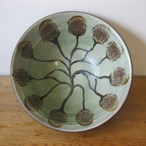 以下が含まれることがあります： 淡い緑色の内側と茶色の縁を持つセラミックボウル。ボウルは、茶色と濃いグレーの様式化された花の模様が特徴で、ユニークな装飾品です。ボウルは丸いです。