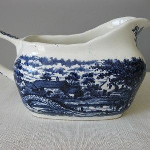 Può includere: Una salsiera in ceramica bianca con un motivo floreale blu e bianco. La salsiera ha un manico e un beccuccio.
