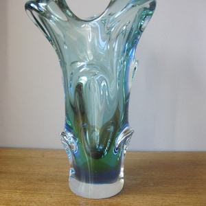 Può includere: Un vaso di vetro blu e verde con una forma organica unica. Il vaso ha un'apertura larga e una base stretta.