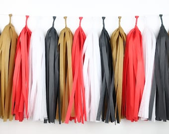 May include: A string of tissue paper tassels in black, white, gold, and red. The tassels are hanging from a white string.