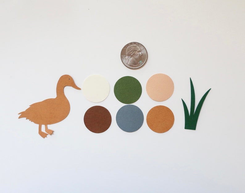 May include: A brown paper duck cutout with a white, brown, green, blue, and beige paper circles and a green paper grass cutout.