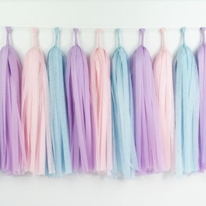 May include: A pastel-colored tassel garland featuring pink, light blue, and lavender tassels. The tassels are made of a lightweight material and are suspended from a white string, perfect for party decorations.