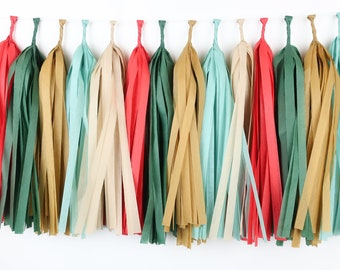 Peut inclure: Une guirlande de pompons en papier colorés, dans des tons de rouge, vert, or, beige et turquoise. Les pompons sont disposés en rangée sur un fond blanc, parfaits pour les décorations de fête ou les travaux manuels.