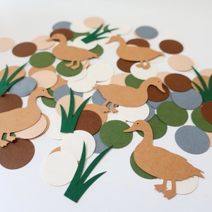 May include: Brown paper duck cutouts with green grass cutouts on a white background. There are also brown, beige, and gray paper circles.