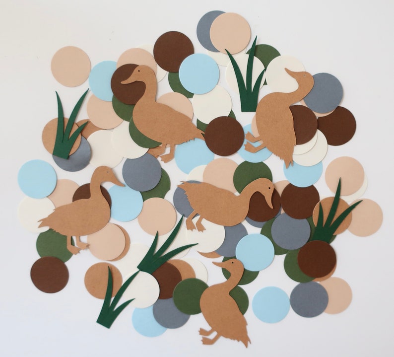 May include: A collection of brown paper duck cutouts with green paper grass cutouts and various colored paper circles in shades of brown, blue, beige, and white.