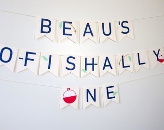 May include: A white banner with blue letters spelling "Beau's O-Fishally One" with fishing-themed illustrations.