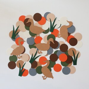 May include: A collection of brown paper ducks and green paper reeds on a white background surrounded by colorful paper circles in shades of brown, orange, white, and gray.