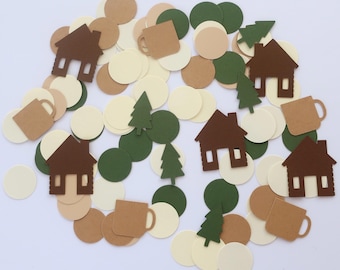 May include: A collection of paper confetti shapes including brown houses, tan mugs, dark green pine trees, and circular discs in shades of cream, tan, and dark green. The assorted die-cut pieces are scattered across a plain white surface.
