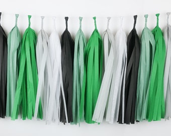 May include: A garland of tissue paper tassels in black, green, and white. The tassels are strung together and hang from a white background.