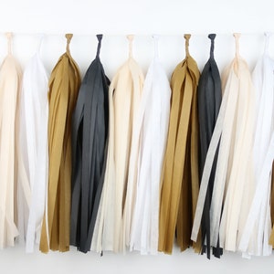 May include: A garland of tissue paper tassels in black, white, and gold. The tassels are strung together on a white string.