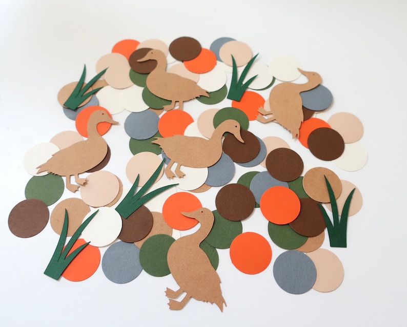 May include: A collection of brown paper duck cutouts on a white background surrounded by various colored paper circles. The circles are in shades of brown, orange, green, gray, and beige.
