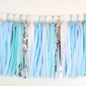 May include: A blue and white tissue paper tassel garland with silver accents. The garland is perfect for a baby shower or birthday party.