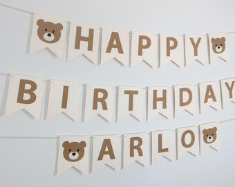 May include: White banner with brown letters spelling "Happy Birthday Arlo" with brown bear faces on each end.