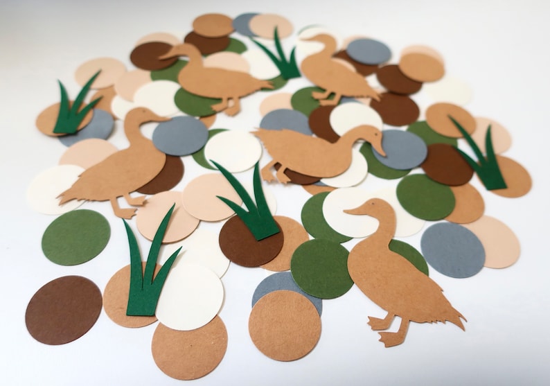 May include: A collection of brown, green, beige, and gray paper circles and duck cutouts. The duck cutouts are brown and have a simple design. The circles are scattered on a white background.