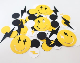 May include: A pile of yellow, black, and white paper confetti with lightning bolt and smiley face designs.