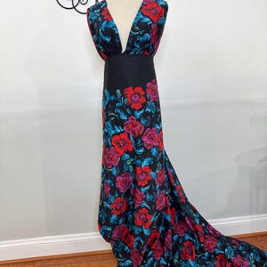 May include: A black dress with a plunging neckline and a long train. The dress is adorned with a vibrant floral pattern featuring red and purple roses with blue leaves. The dress is displayed on a mannequin.