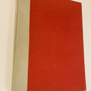 May include: A red hardcover book with a white spine. The book is closed and the spine is visible.