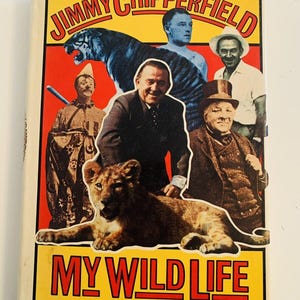 May include: A book cover with a yellow background and the title "My Wild Life" in red letters. The cover features a photo of Jimmy Chipperfield, a famous circus performer, with a lion cub. Other circus performers and animals are also pictured on the cover.