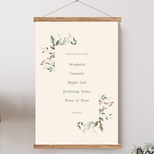 May include: A framed wall art print with a cream background and text that reads "AND HE WILL BE CALLED" followed by "Wonderful, Counselor, Mighty God, Everlasting Father, Prince of Peace." The print is decorated with green leaves and red berries.