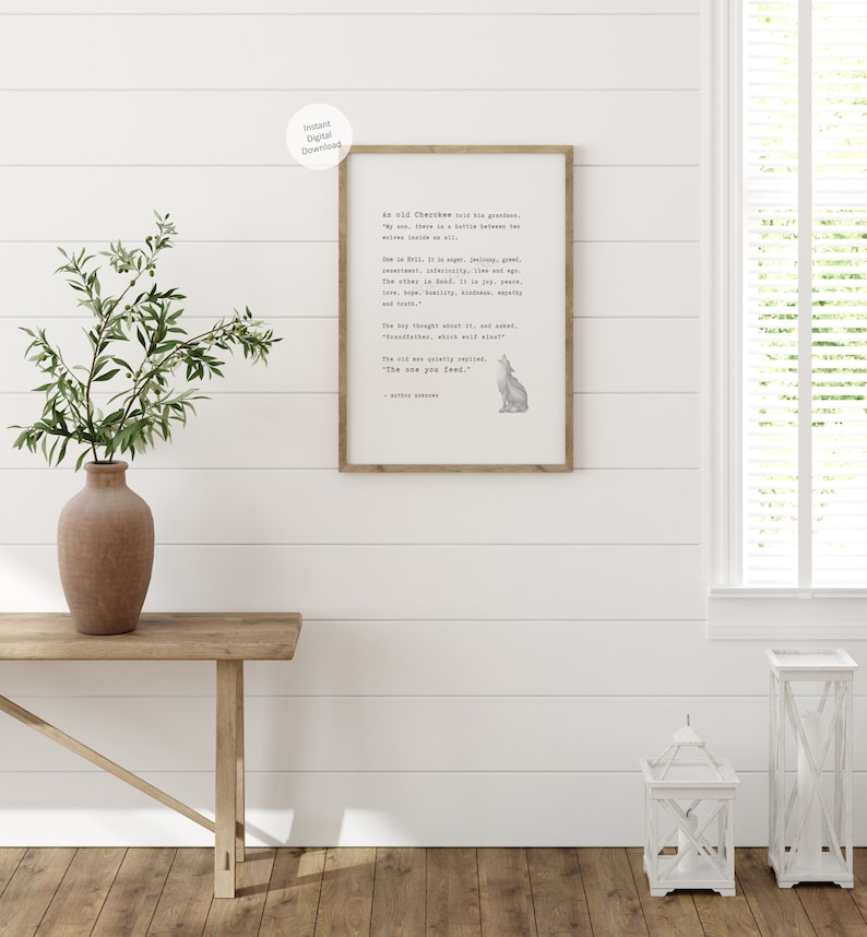 May include: A framed print with a quote about two wolves, with a watercolor illustration of a howling wolf. The print is in a wooden frame and is displayed on a white wall. The text reads "The one you feed."