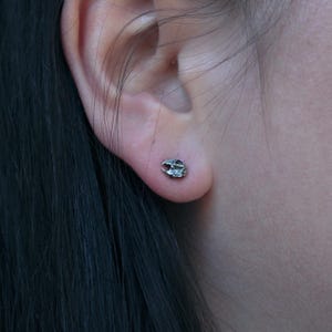 May include: A pair of small, silver stud earrings in the shape of a skull.