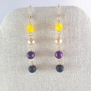 Op de afbeelding: Een paar gouden oorhangers met gele, witte, paarse en zwarte kralen.