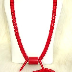 May include: A red beaded necklace and two matching bracelets. The necklace has a large red bead in the centre and two small spikes on either side. The bracelets are simple circles of red beads.