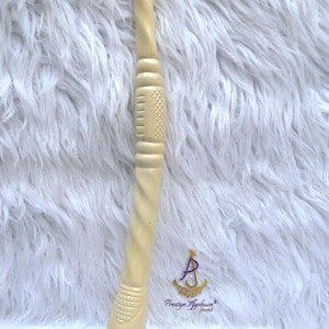 May include: A cream-coloured, elongated, carved object with a twisted, textured shaft and a wider, patterned base. The object features intricate geometric engravings and horizontal bands along its length, with the text Prestige Applause Jewels.