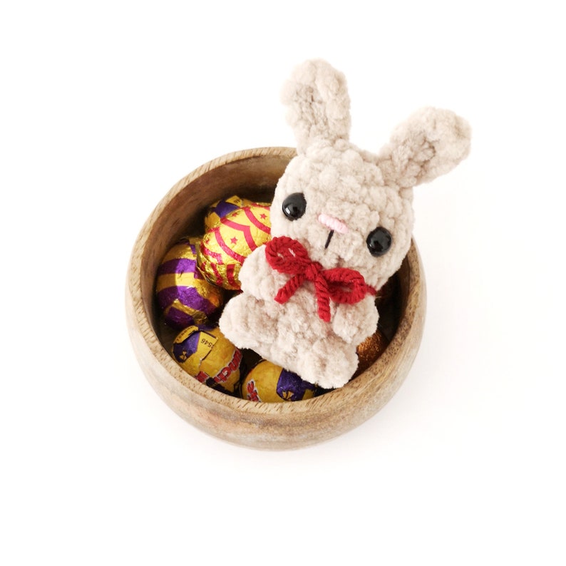 May include: A plush brown bunny rabbit with a red bow sits in a wooden bowl filled with foil-wrapped chocolate Easter eggs.