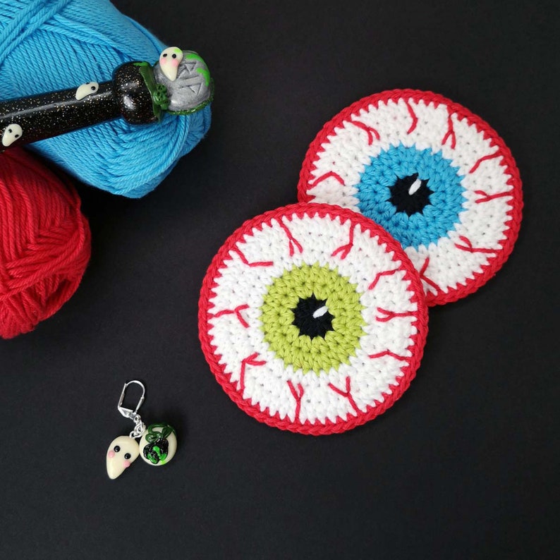 May include: Two crocheted eye coasters in red, white and blue. The eyes are green, blue and black.