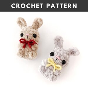May include: Two crocheted bunny plushies, one in beige with a red bow and the other in gray with a yellow bow.