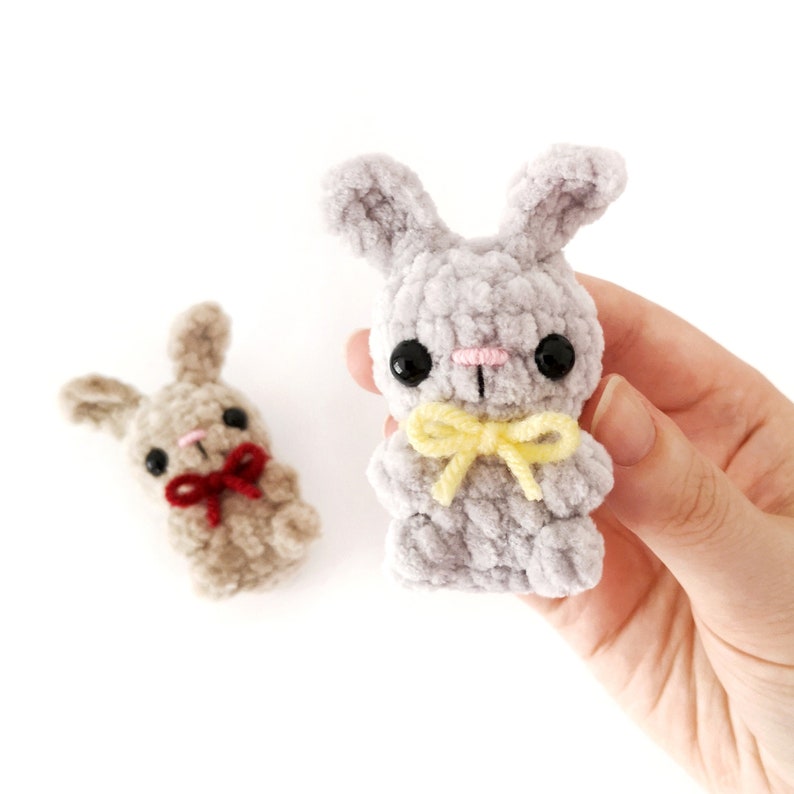 May include: Two crocheted bunny plushies. One is gray with a yellow bow and the other is brown with a red bow.