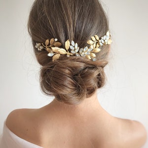 Op de afbeelding: Gouden haar kam met delicate bladeren en heldere kristallen. De kam wordt gedragen in het haar van een vrouw, wat een romantische en elegante look creëert.