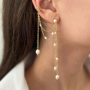 May include: Gold ear cuff with a dangling chain and pearl accents. The chain has multiple strands with small pearls hanging from each strand.