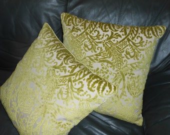 May include: Two decorative throw pillows with a green and white damask pattern. The pillows are on a dark brown leather couch.