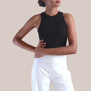 以下が含まれることがあります： 黒いノースリーブのクロップトップと白いワイドレッグパンツを着用した女性