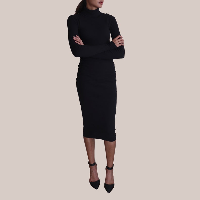 May include: A black turtleneck dress with long sleeves and a fitted silhouette. The dress is knee-length and the model is wearing black heels.