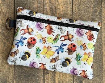 May include: White zippered pouch with a colourful bug print. The print features ladybugs, butterflies, dragonflies, bees, and other insects.