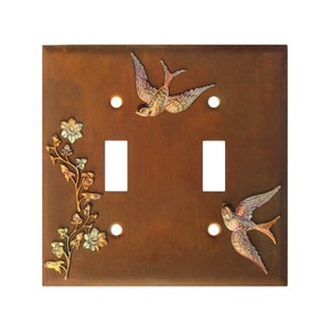 May include: A double light switch cover with a rustic brown finish. The cover features two stylized birds in flight and a floral design in gold and green.