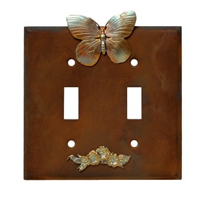 May include: A double light switch cover with a rustic brown finish. The cover features a decorative butterfly and floral design in gold and silver.