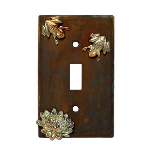 May include: A rusty brown metal light switch cover with a gold frog, a gold frog, and a gold flower design.