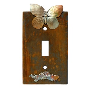 May include: Rustic light switch cover with a butterfly and floral design. The cover is made of metal with a rusty finish.