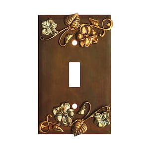 May include: A light switch cover with a decorative floral design. The cover is made of metal and has a rustic brown finish. The flowers are gold and green.