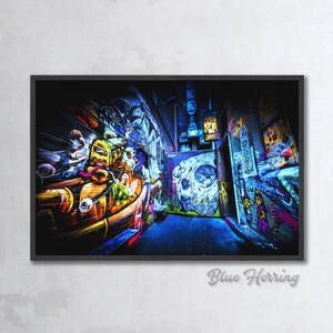 May include: A narrow alleyway with colorful graffiti art on the walls. The walls are covered in bright colors, including yellow, blue, green, and red. The graffiti includes abstract shapes, letters, and a skull design.